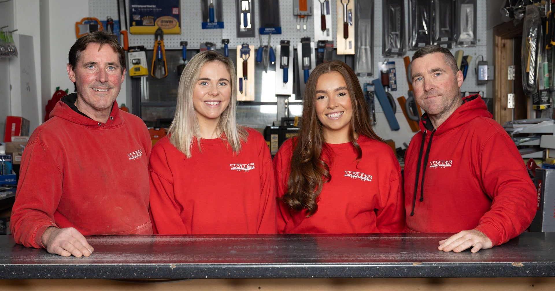 Four individuals in red uniforms standing behind a counter in a workshop.