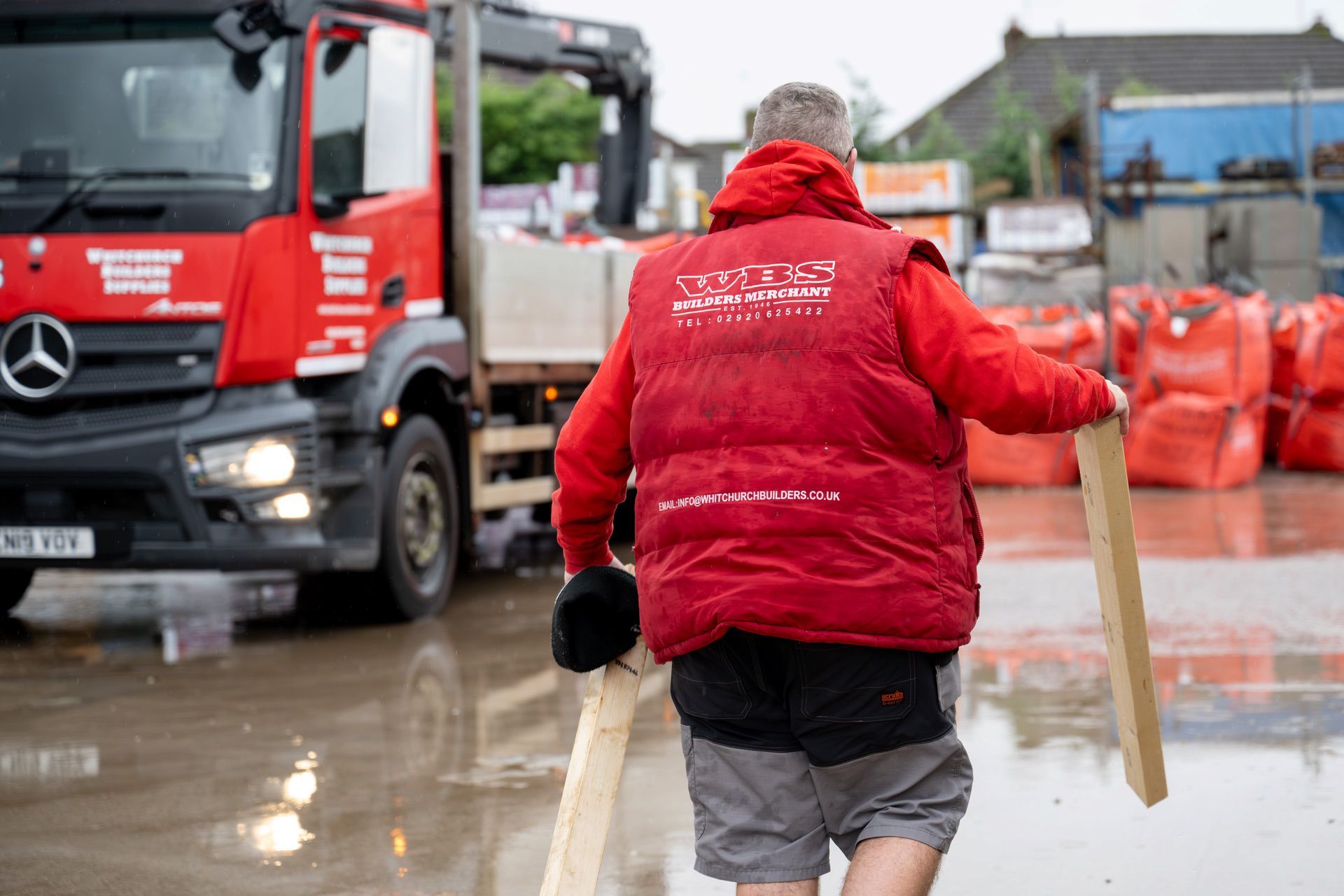 A man in a red jacket walking through a puddle.