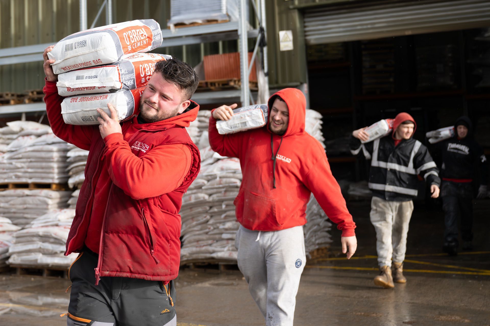 Workers carrying heavy bags on their shoulders at an industrial site.