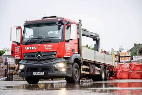 Red mercedes-benz truck with crane arm parked at a construction supply site.