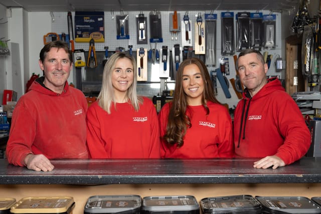 Four people in red shirts standing in front of a shop.