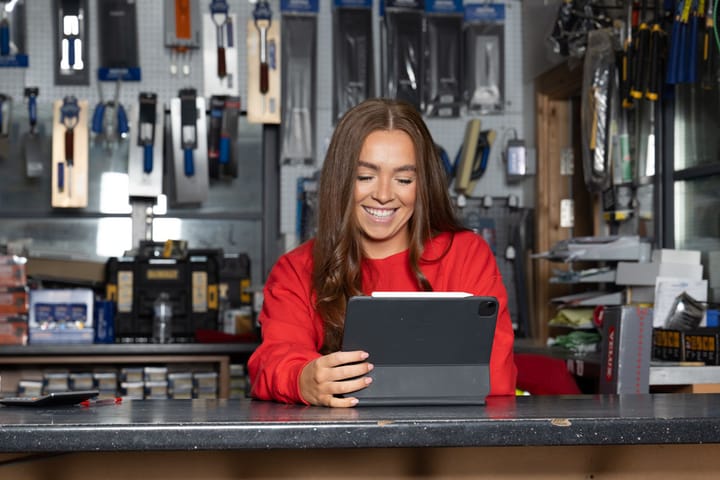 A woman smiling at a tablet in a shop.
