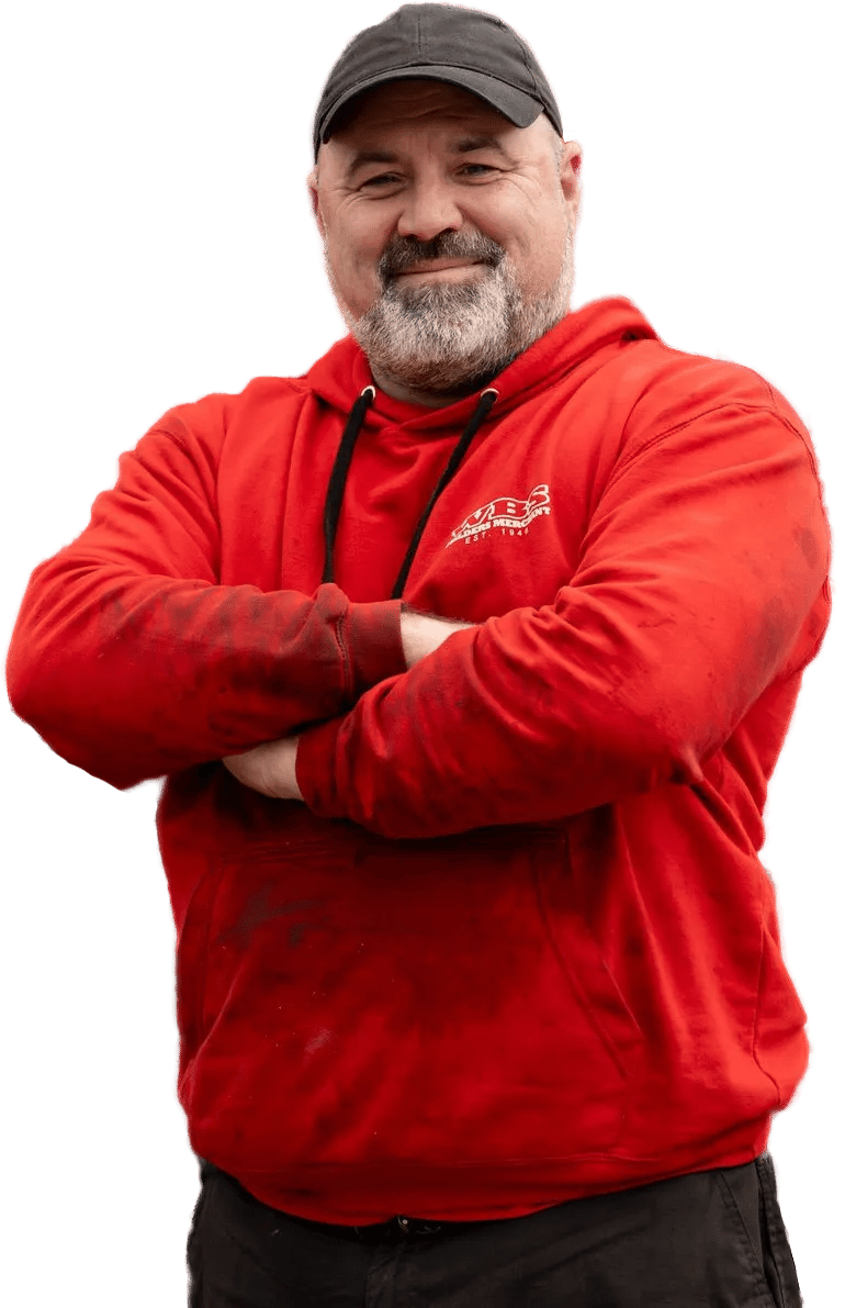 Man in a red hoodie and black cap stands with arms crossed, smiling.