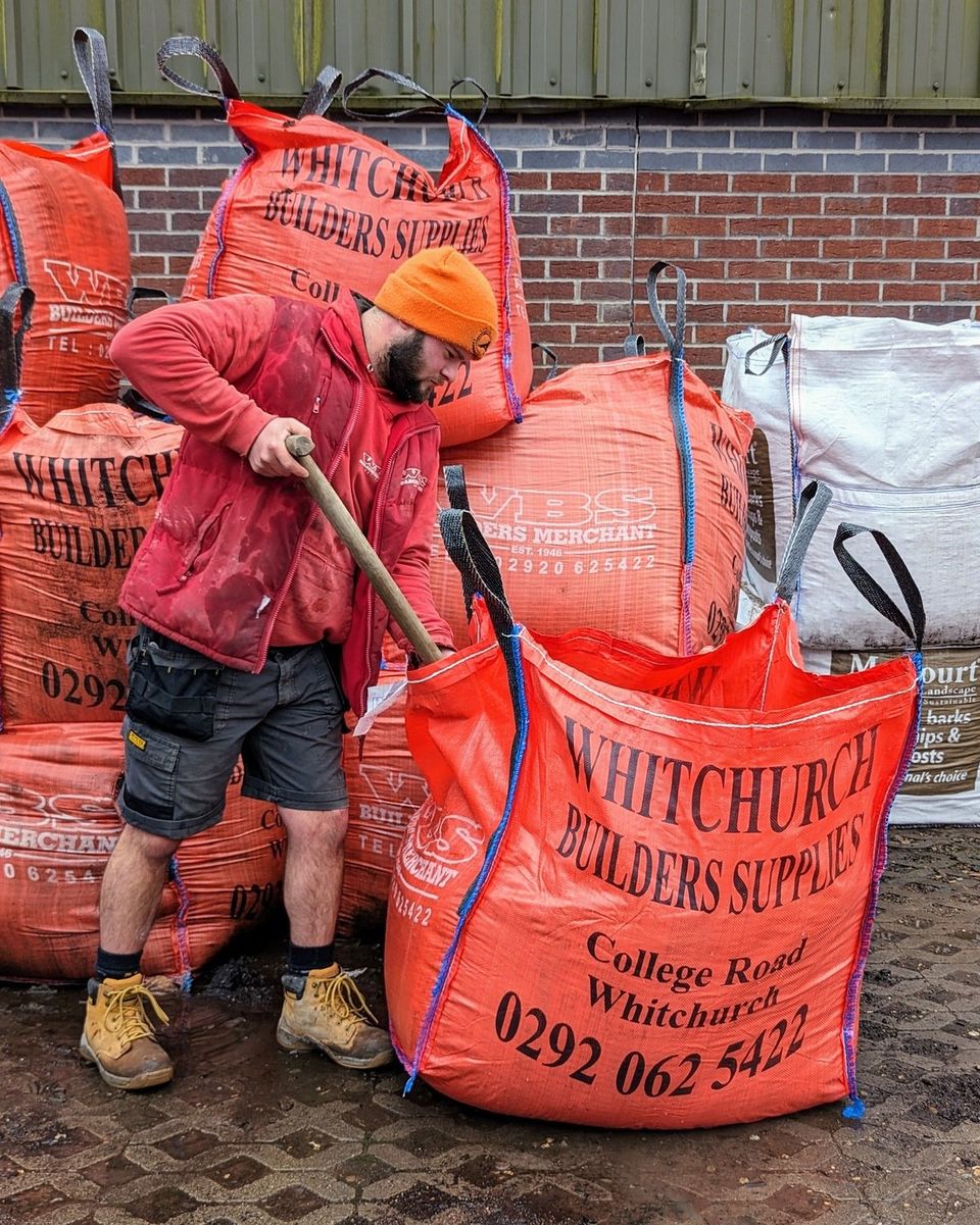 Man in workwear shoveling material from a large bulk bag.