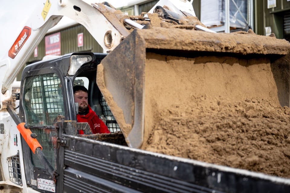 Construction worker operating a skid steer loader to move sand.
