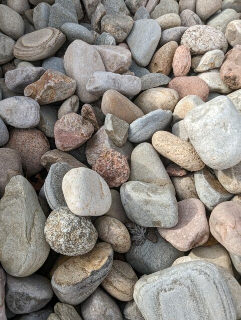 A variety of smooth, rounded stones in different sizes and shades of gray, beige, and pink are piled together.