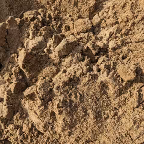 Close-up of a pile of brown sand with coarse texture and irregular clumps.