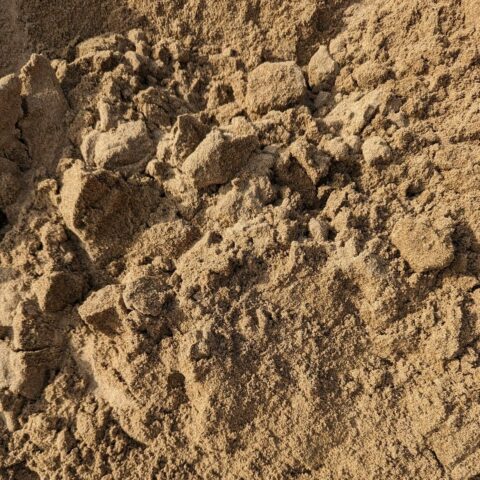 Close-up of a pile of brown sand with coarse texture and irregular clumps.