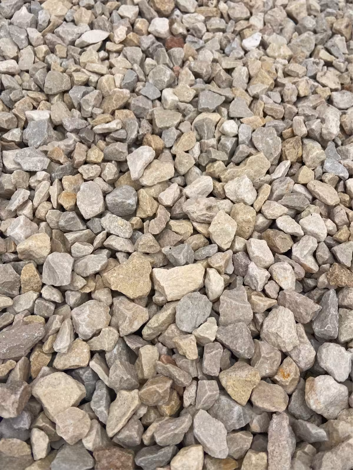A close-up of Cotswold Buff Chippings (20mm), showcasing variously sized small gray and beige gravel stones.