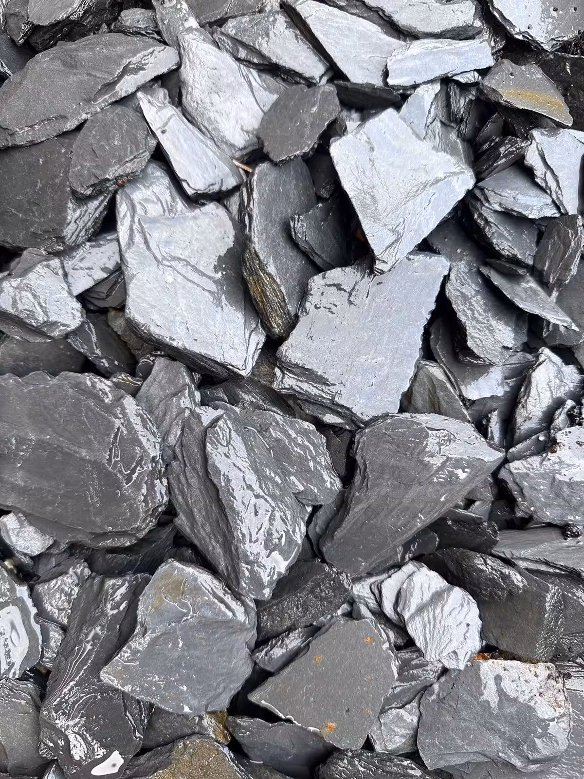 A pile of Natural Slate Chippings in dark gray, featuring sharp edges and shiny surfaces.