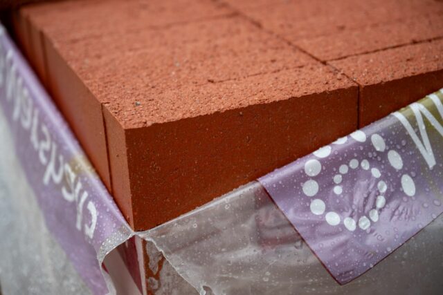 A stack of red bricks covered by a translucent plastic sheet with white patterns.