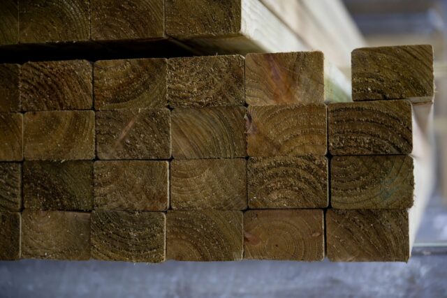 A stack of cut lumber beams with visible growth rings, neatly arranged in a pile.